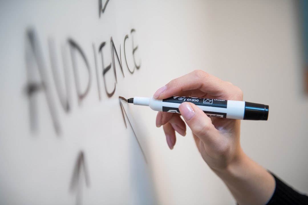 Womans hand writing the word audience on a whiteboard, with arrows.